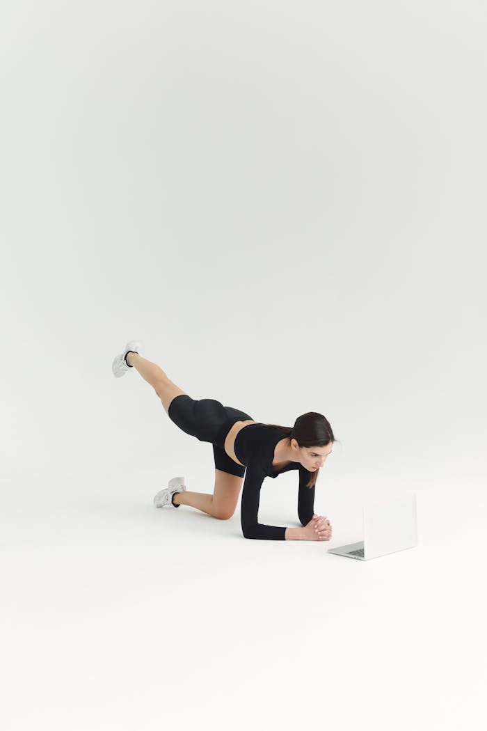 Woman performing a fitness workout indoors, using a laptop for guidance. Bright, minimal setting.