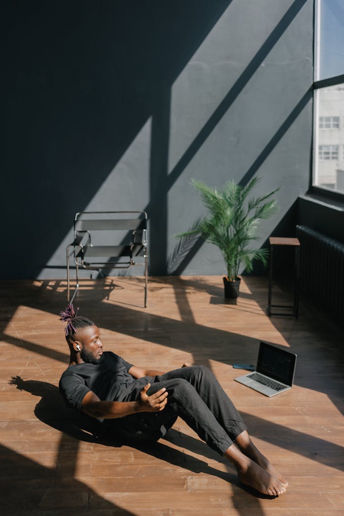 Adult man exercising on wooden flooring indoors, using a laptop for guidance.
